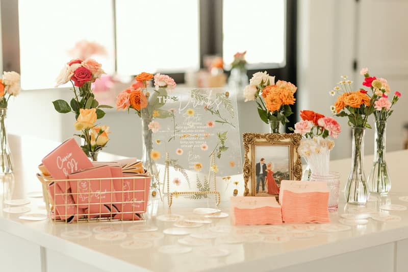 Bar welcome table dressed with bright florals and personalised koozies