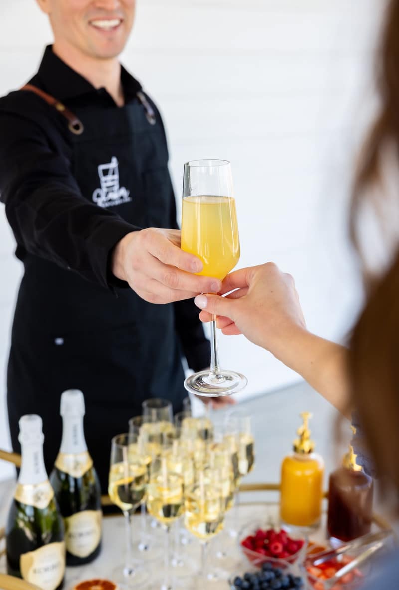 Shaker bartender handing a mimosa across the bar