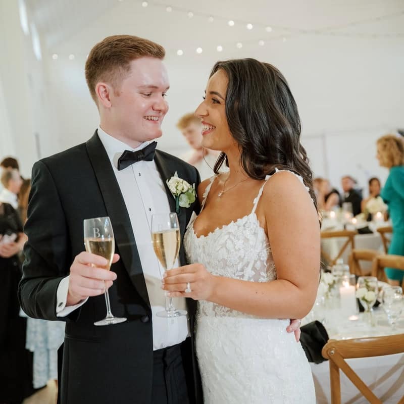 Bride and groom smiling at each other over champagne flutes at their reception