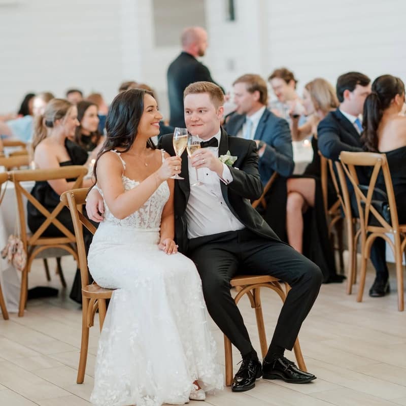 Bride and groom seated together with champagne flutes as their guests dine behind them