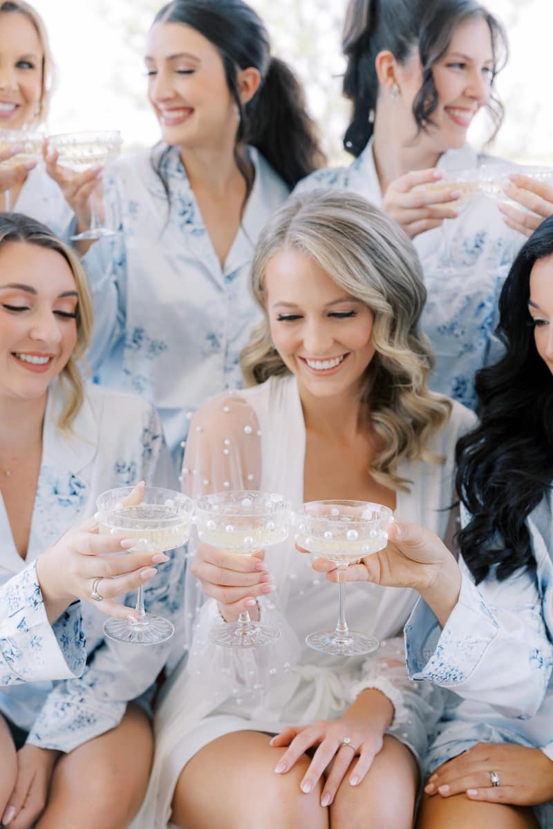 Bridesmaids in matching robes toasting with champagne coupes
