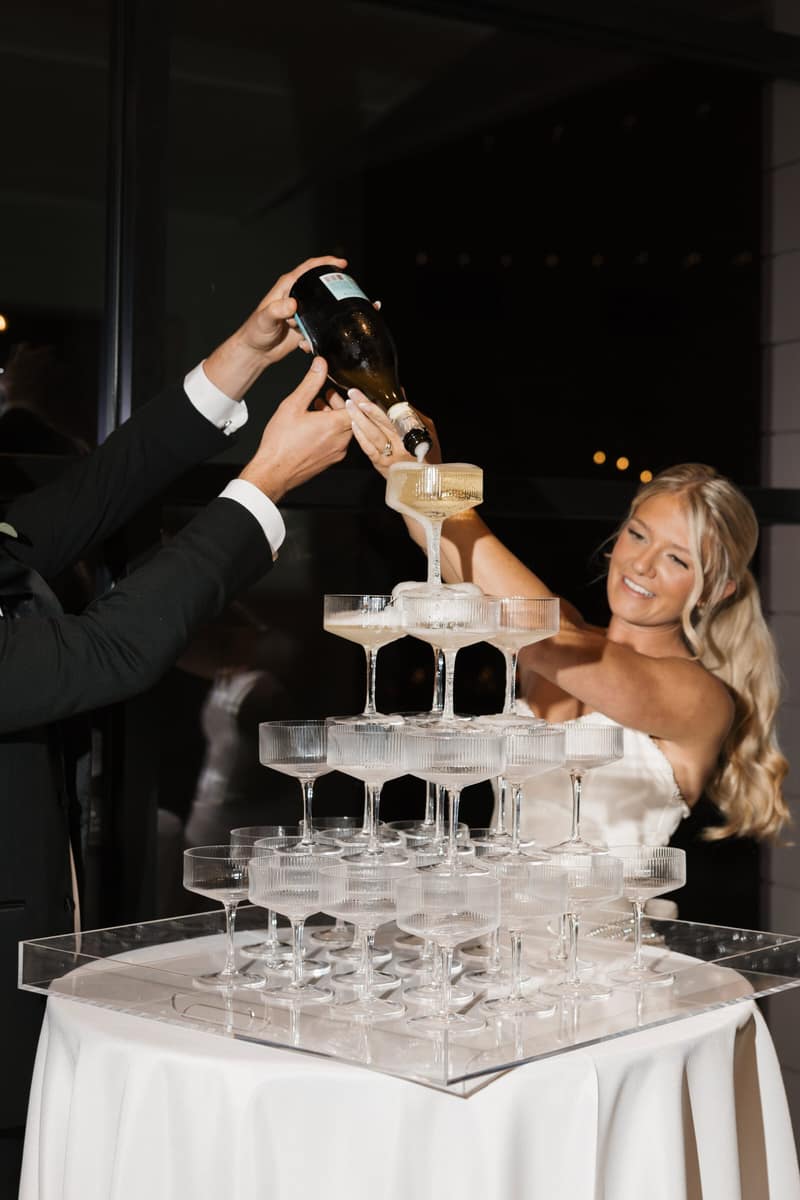 Champagne being poured into a coupe tower while the bride watches