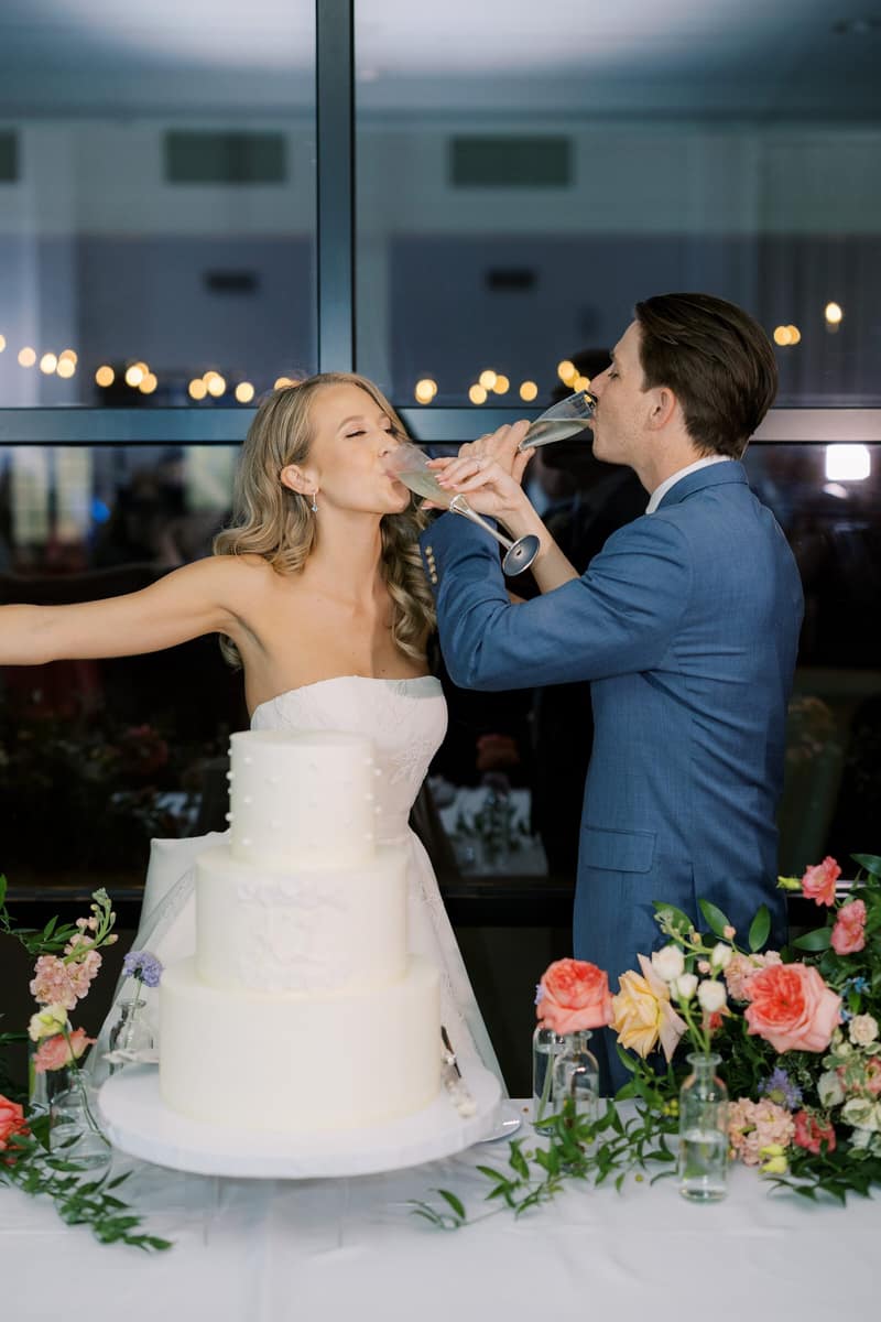 Couple drinking champagne beside their wedding cake