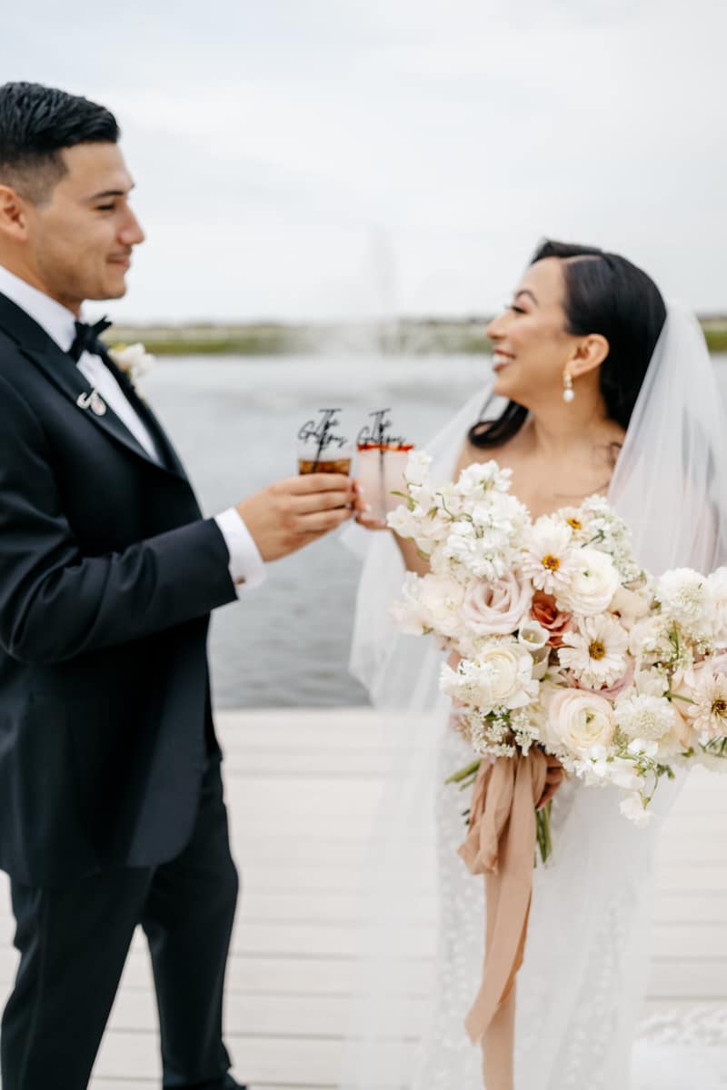 Bride and groom toasting champagne flutes outdoors beside the water