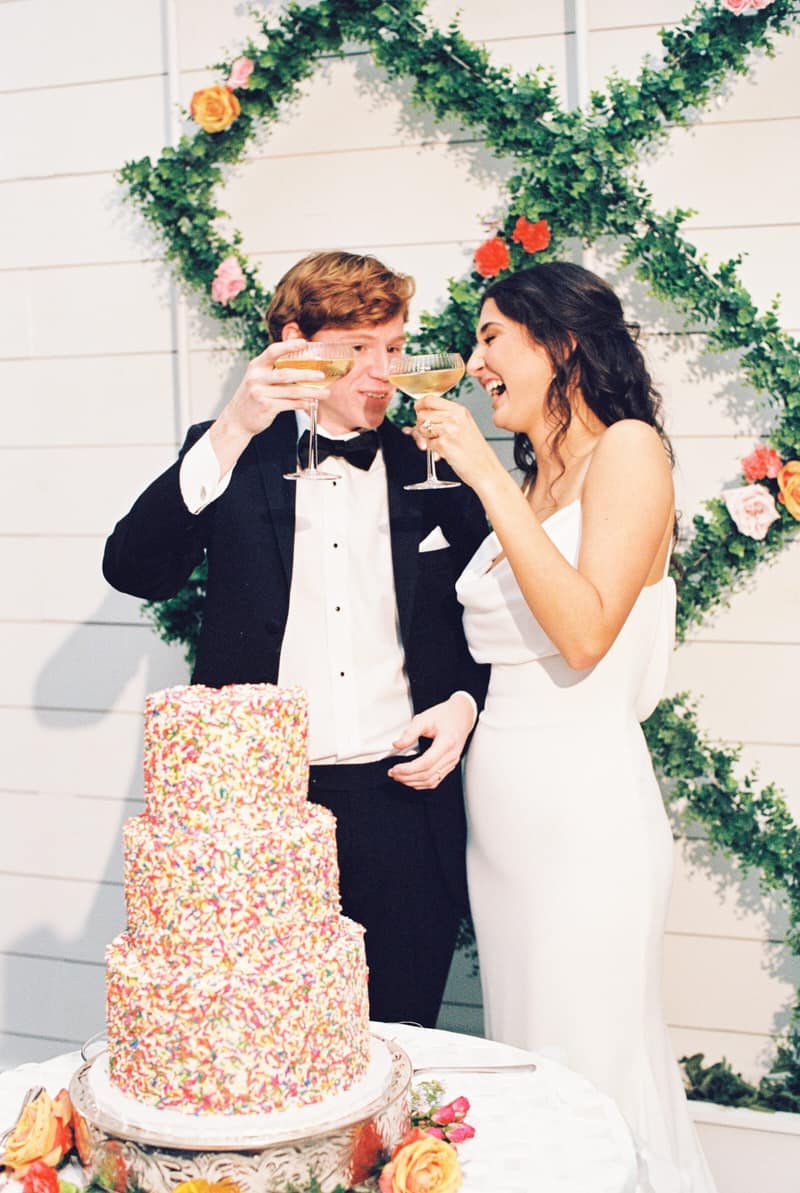 Couple toasting with champagne beside their wedding cake
