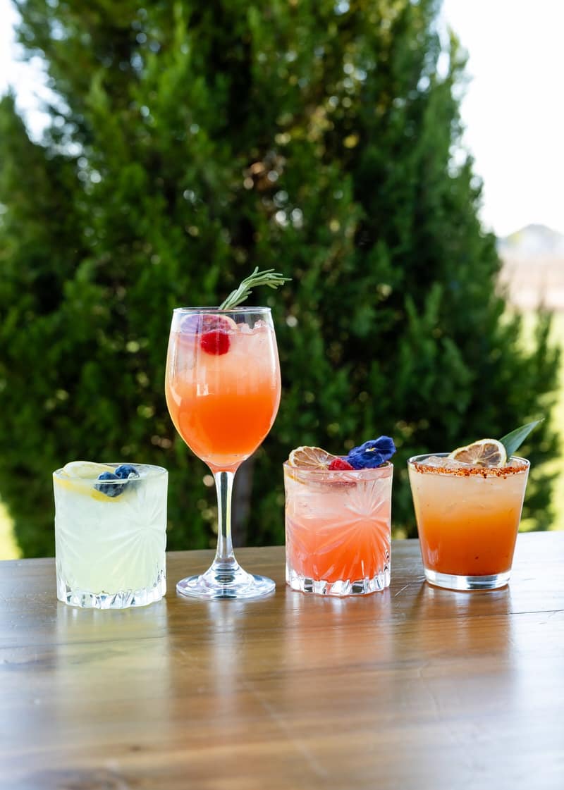 Four signature cocktails lined up on a wooden table outdoors