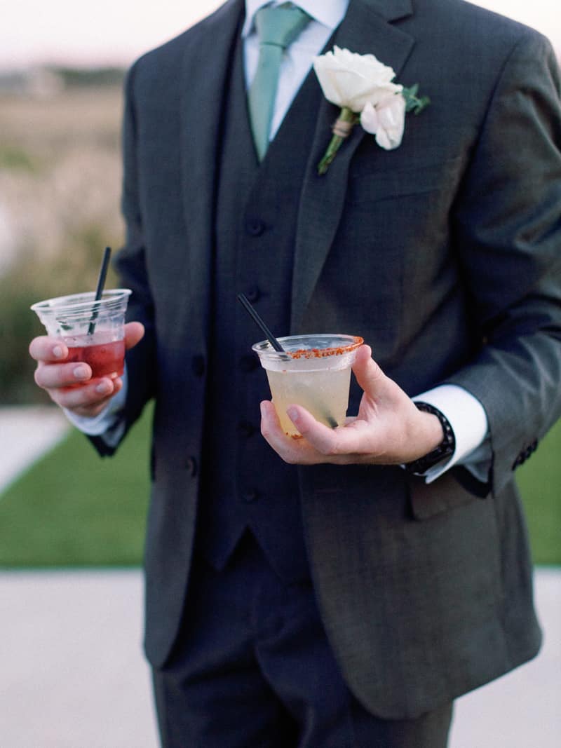 Groom carrying two garnished cocktails from the bar