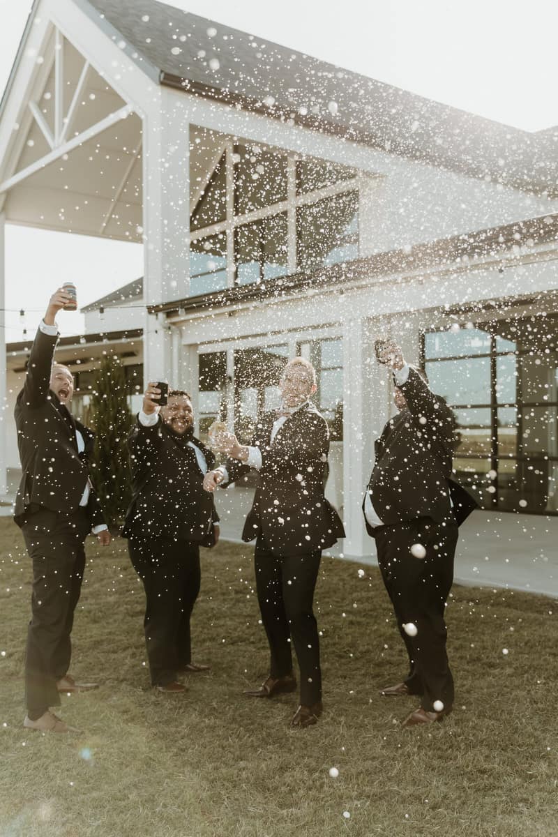 Groomsmen celebrating outside a white barn wedding venue