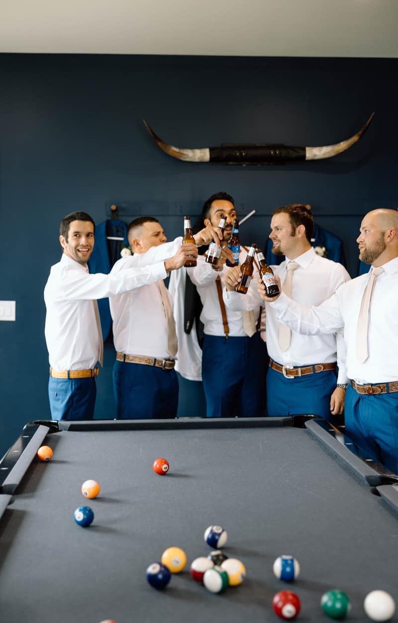 Groomsmen toasting with beers around a pool table