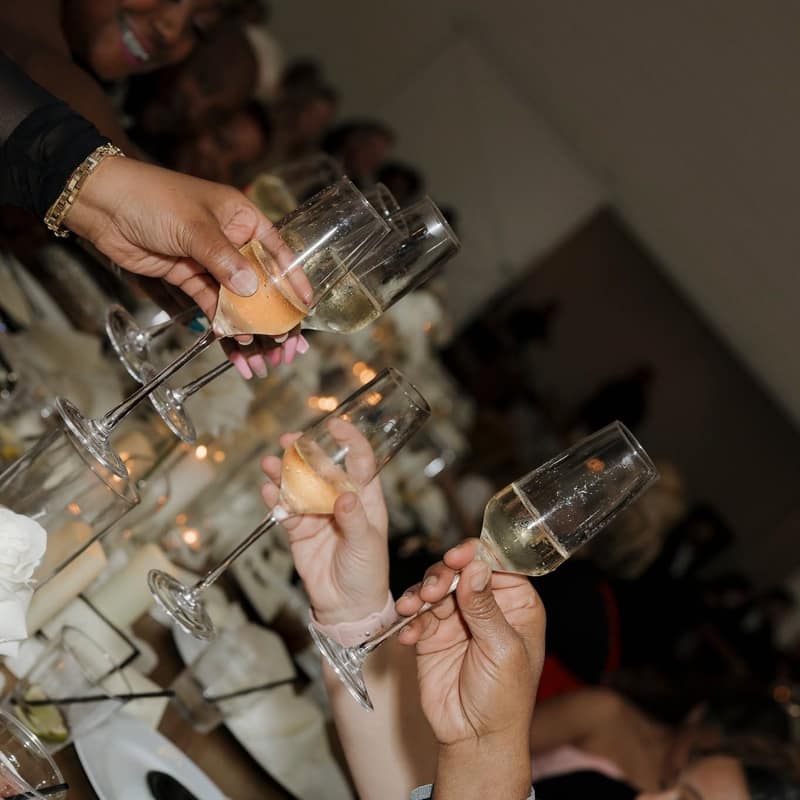 Hands passing wine and champagne glasses across a reception table during a toast