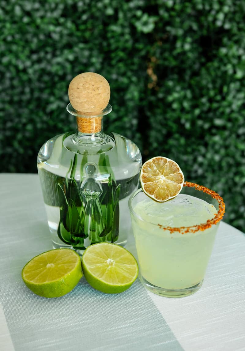 Margarita served with fresh limes beside a bottle of tequila
