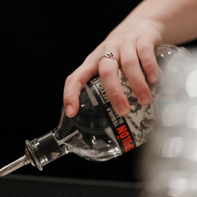 Bartender's hand tipping a tequila bottle fitted with a pour spout over a glass