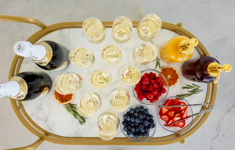 Mimosa bar cart with champagne coupes, fruit juices and fresh berries