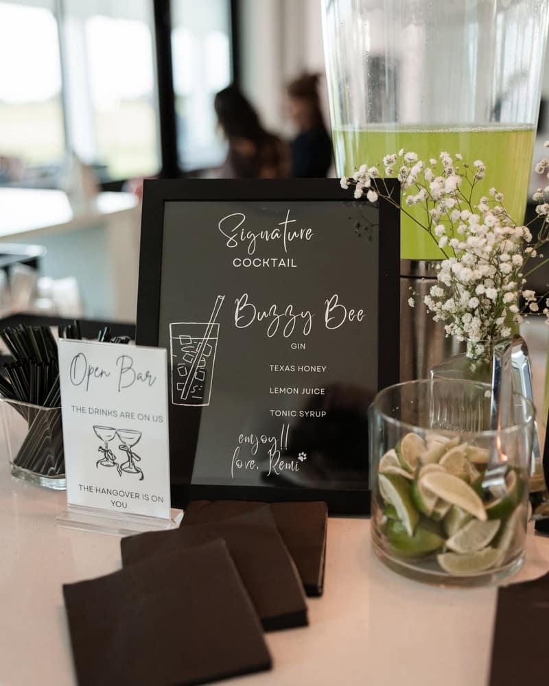 Signature cocktail card and an open bar sign on the bar beside a jar of cut limes