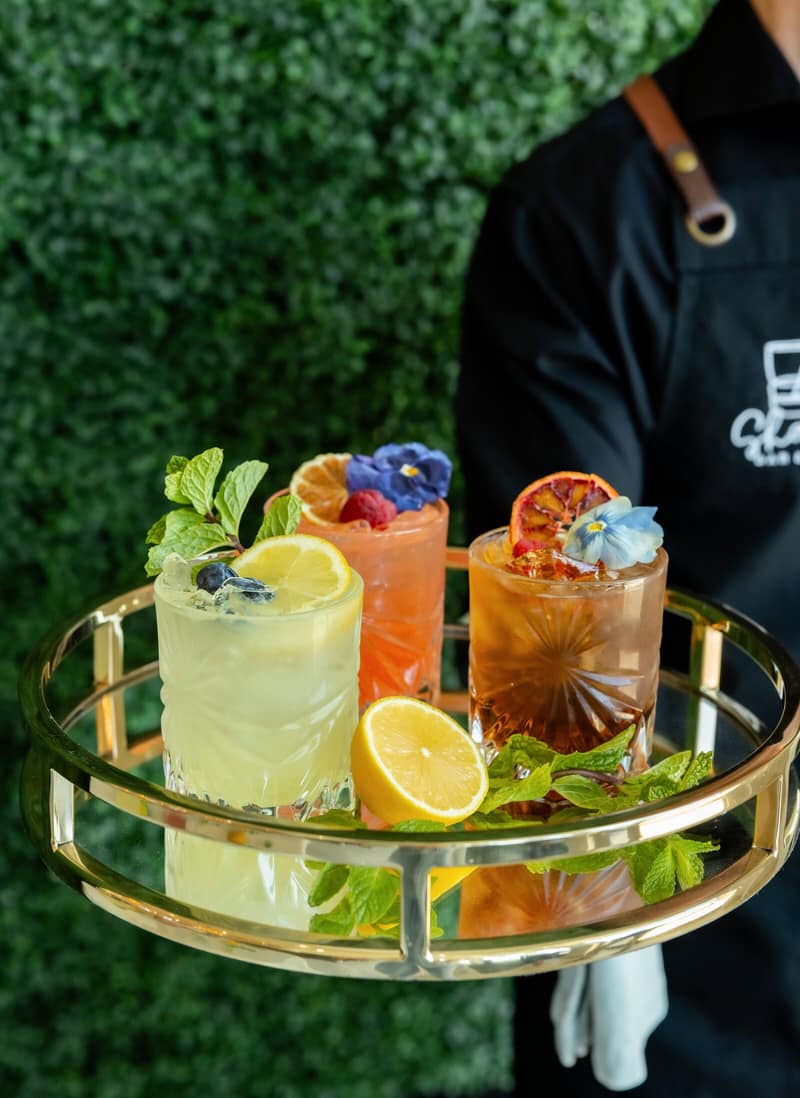 Bartender presenting a gold tray of garnished signature cocktails