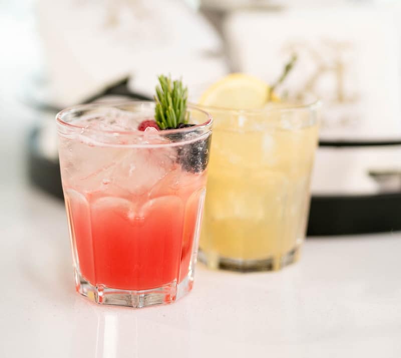 A pink and a yellow signature cocktail garnished with rosemary
